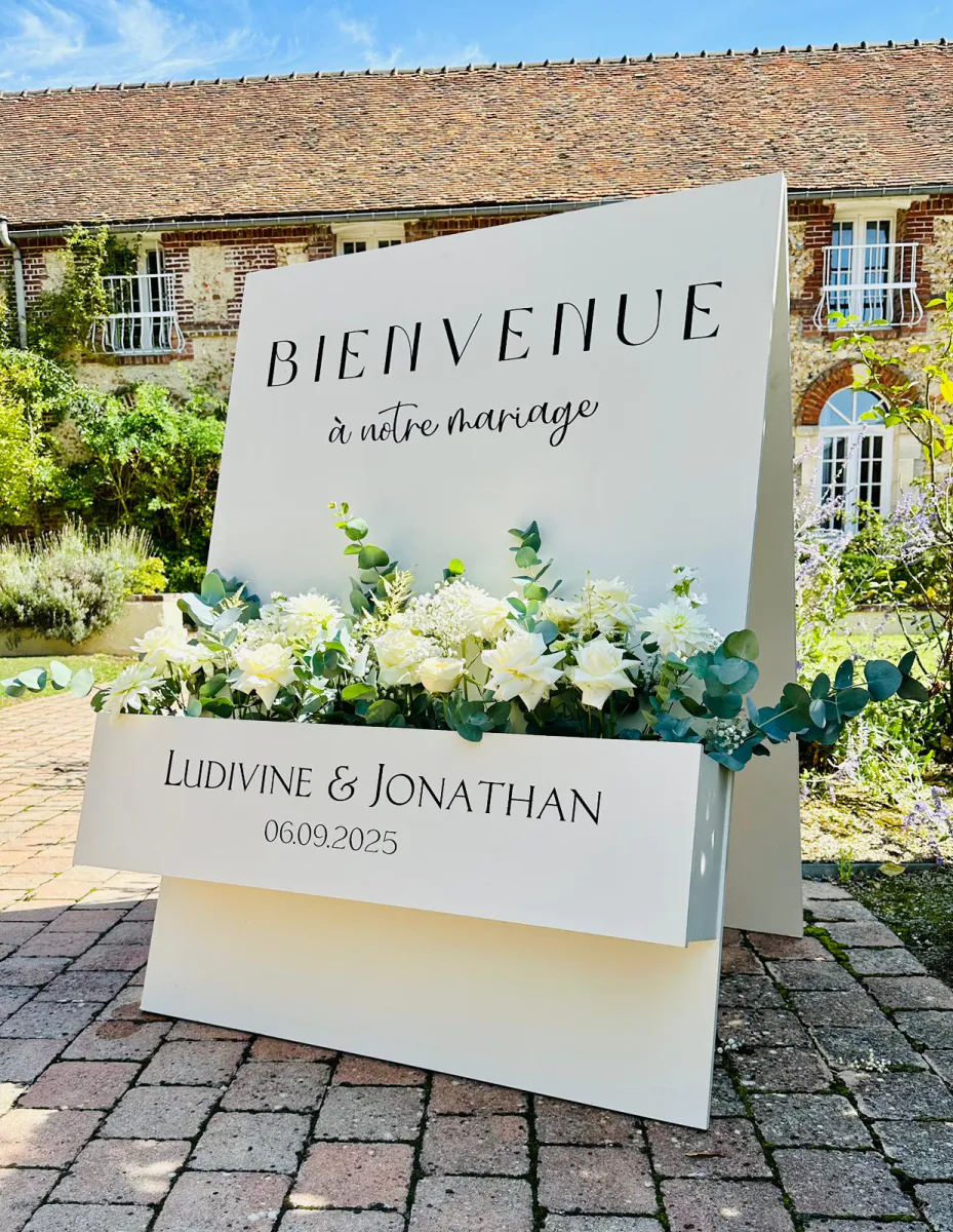 Panneau de bienvenue fleuri devant une bâtisse ancienne