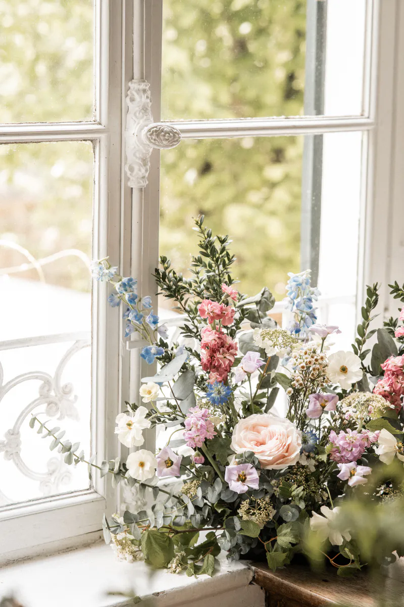 Composition florale bleue et rose devant une fenêtre