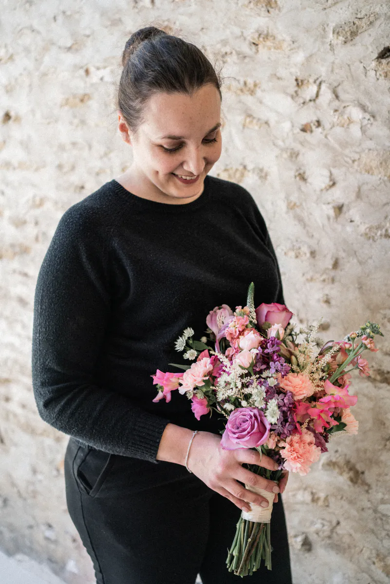Mélissa Lois avec un bouquet de mariée devant un mur de pierre