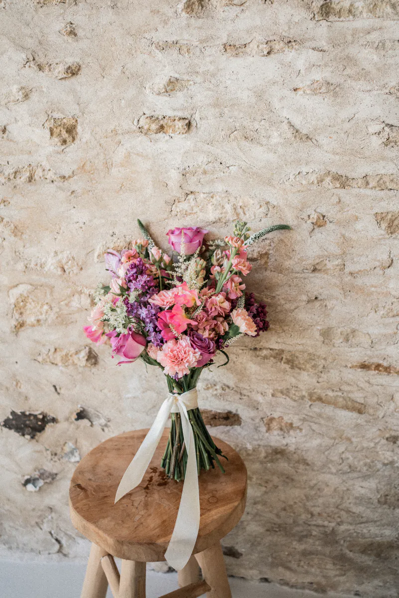 Bouquet noué de rubans posé sur un tabouret, devant un mur de pierre