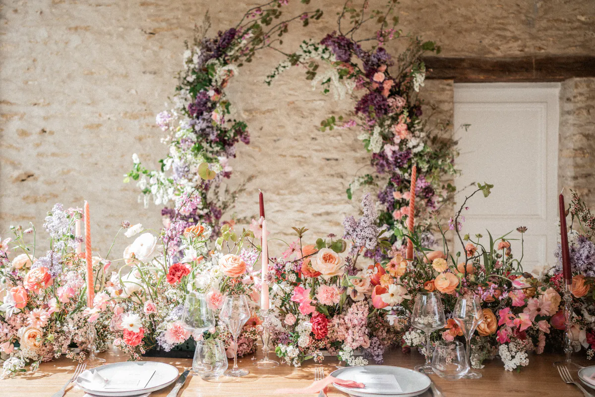 Arche florale foisonnante au-dessus d'une table, devant un mur de pierre