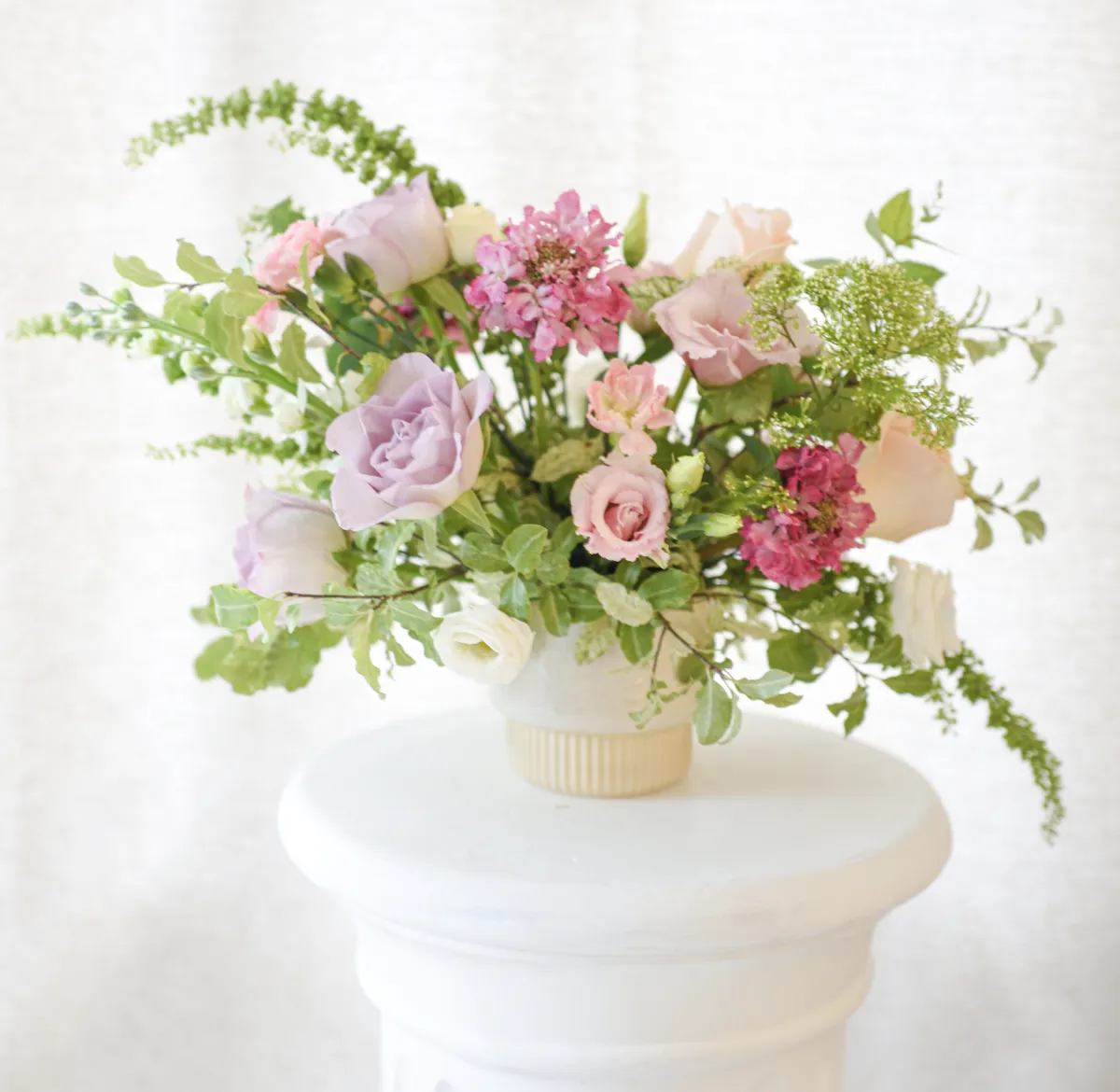 Composition florale pastel posée sur une colonne blanche