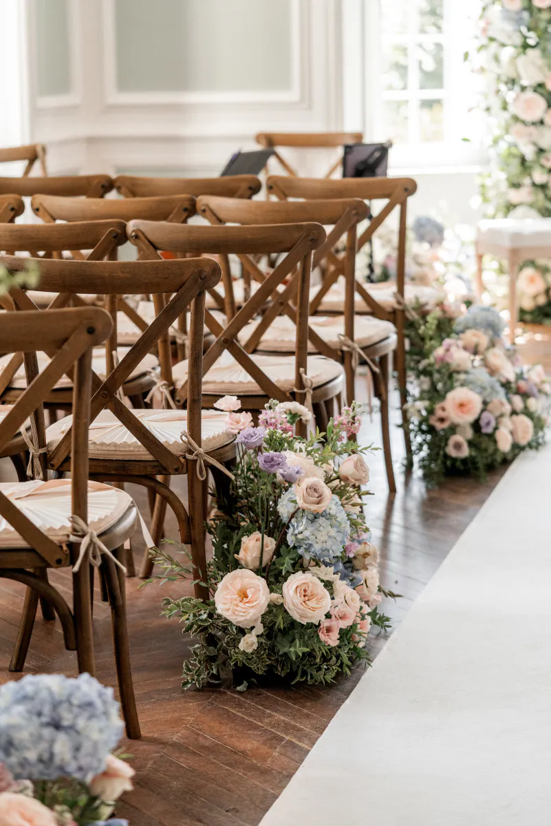 Allée de cérémonie fleurie entre des chaises en bois