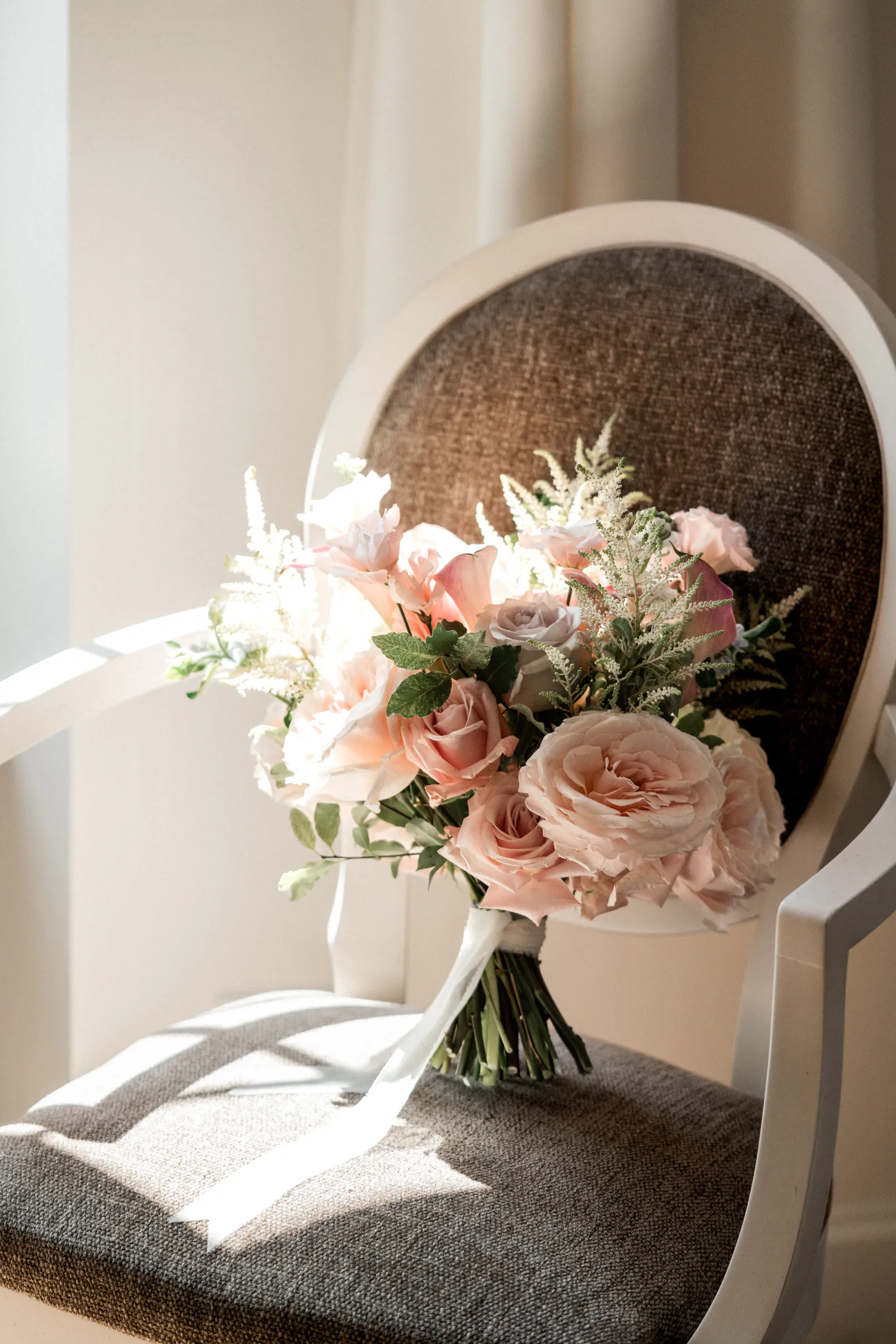 Bouquet de mariée aux roses poudrées posé sur un fauteuil médaillon