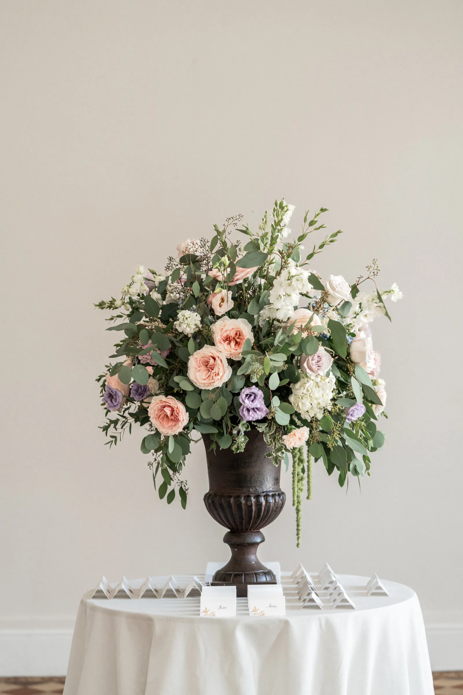 Composition florale aux roses poudrées dans une vasque noire, sur une table ronde d'un salon lumineux
