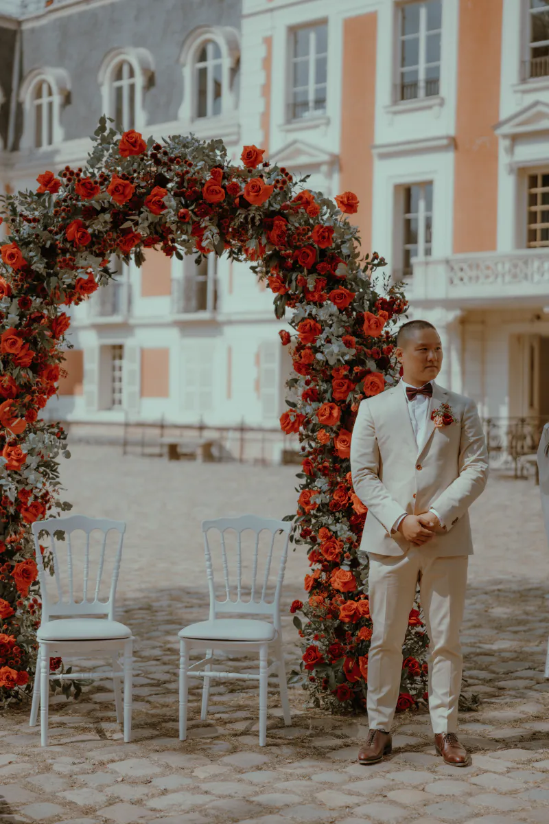 Marié attendant devant une arche de roses rouges dans la cour d'un château