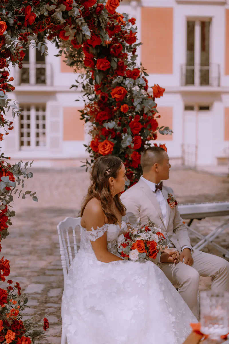 Mariés assis sous l'arche de roses rouges pendant la cérémonie