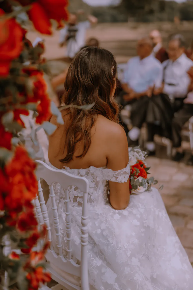 Mariée de dos pendant la cérémonie, encadrée de roses rouges