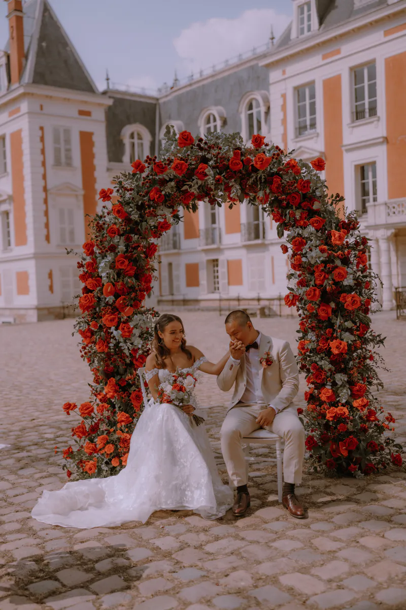 Mariés sous l'arche de roses rouges dans la cour pavée du château