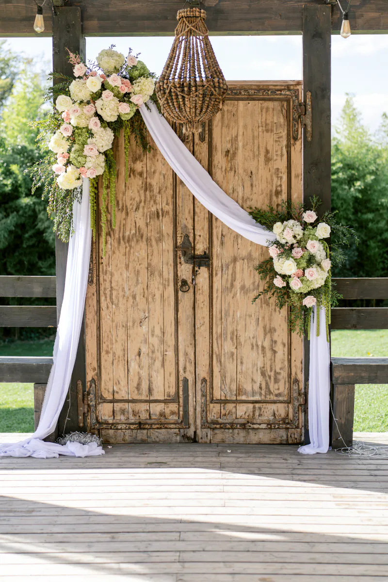 Porte ancienne en bois habillée de voilages et de roses blanches pour une cérémonie laïque