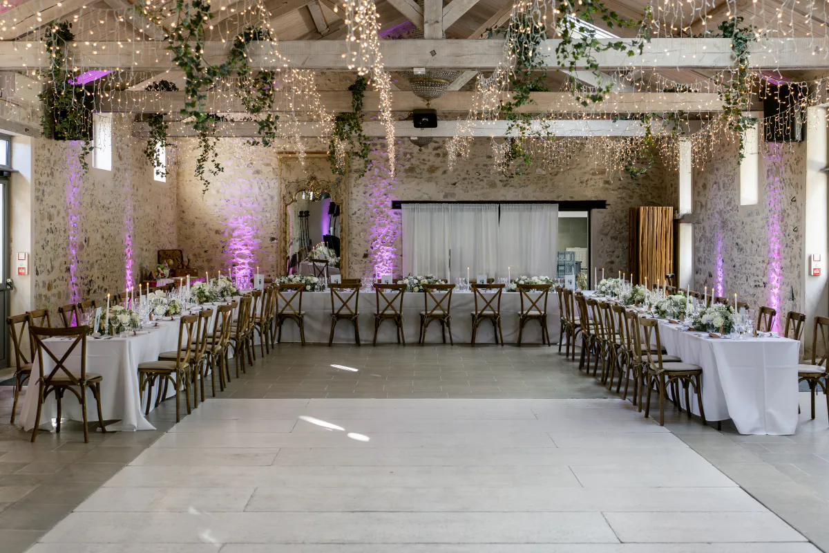 Salle de réception aux poutres apparentes, guirlandes lumineuses et tables dressées